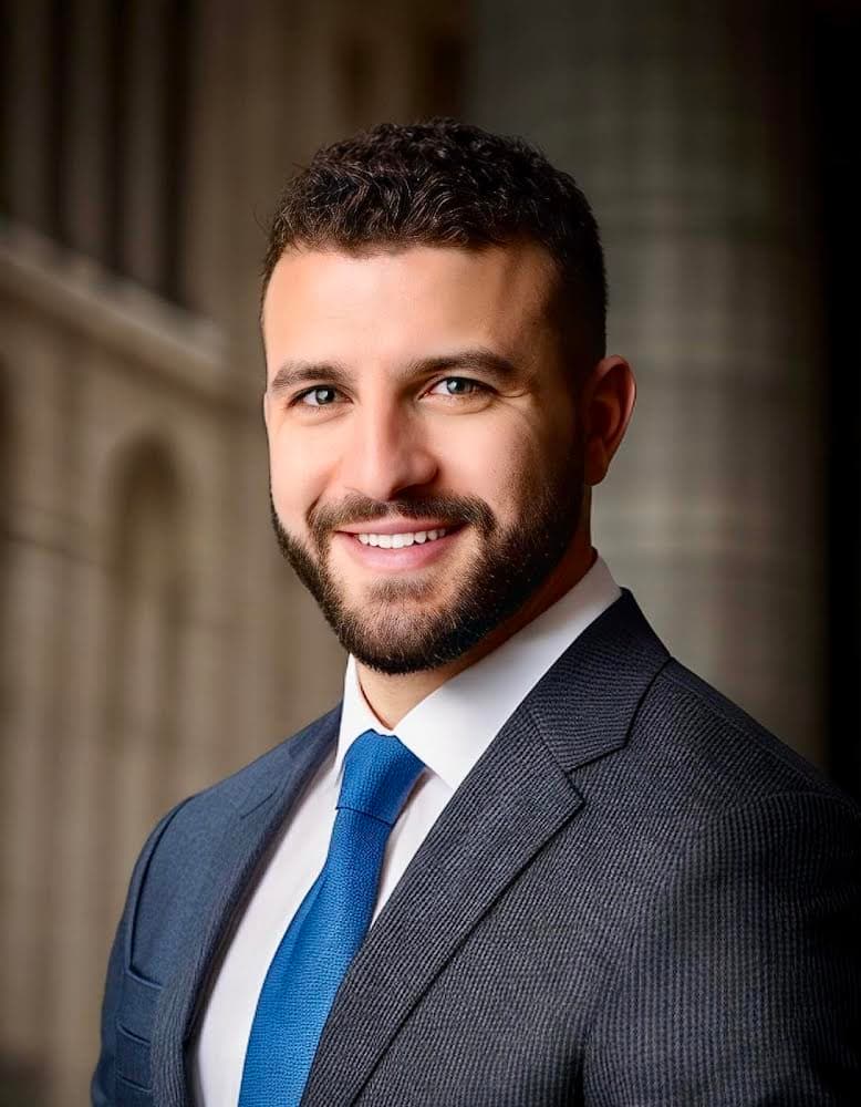 Portrait of Alex Abushanab in a charcoal suit and blue tie